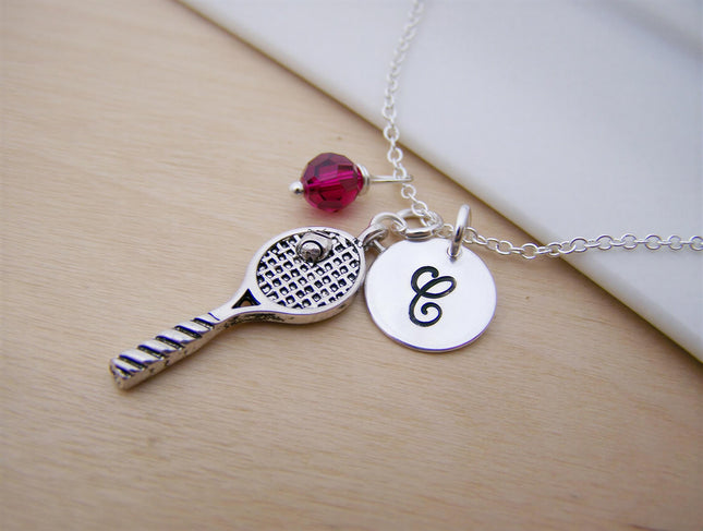 Silver tennis racquet necklace with a pink bead and a round charm printed with the letter C on a thin metal chain.