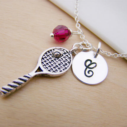 Silver tennis racquet necklace with a pink bead and a round metal charm engraved with the letter C.