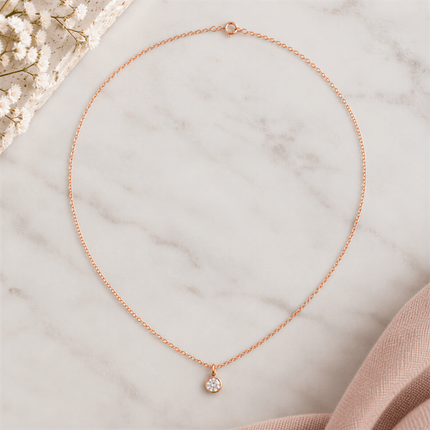 Rose gold chain necklace with a round clear stone pendant on a white marble surface.