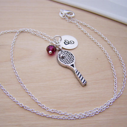 Silver chain necklace with a metal tennis racquet pendant, a pink bead, and a round charm engraved with the letter E.