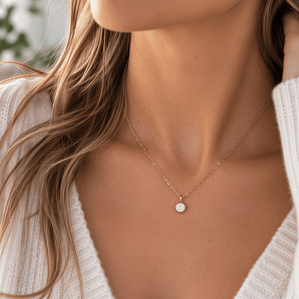 A round clear stone pendant on a rose gold chain worn by a person in a white knit sweater.
