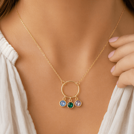 Gold chain necklace with a circular pendant featuring three round blue, green, and purple stones worn on a person.