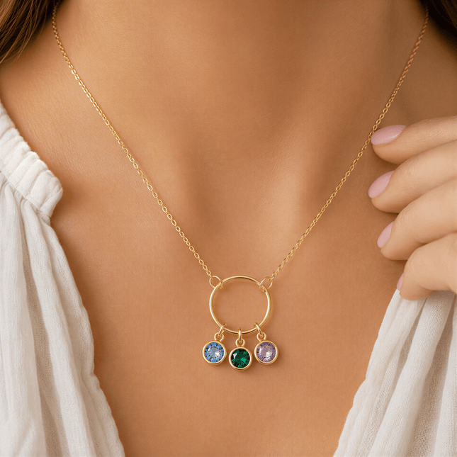 Gold chain necklace with a circular pendant featuring three round blue, green, and purple stones worn on a person.