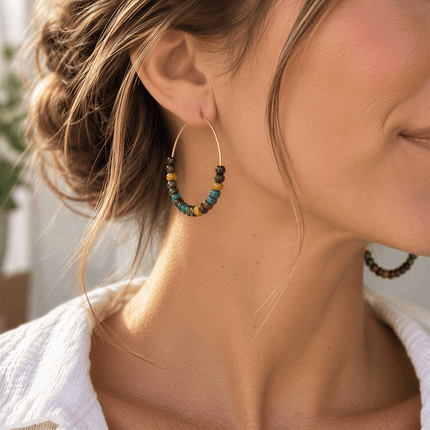 A person wearing a gold hoop earring featuring small, round multicolored glass beads in blue, green, yellow, and brown.