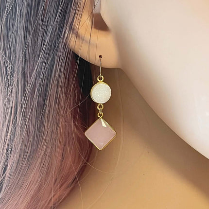 Gold drop earring with a round white druzy and a pink square gemstone worn on a mannequin ear.