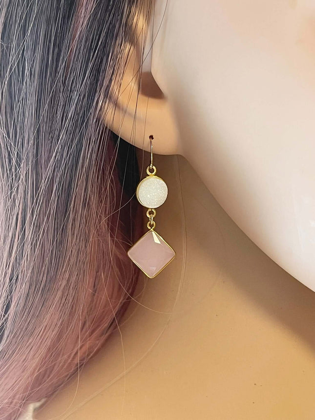 Gold drop earring with a round white druzy and a pink square gemstone worn on a mannequin ear.