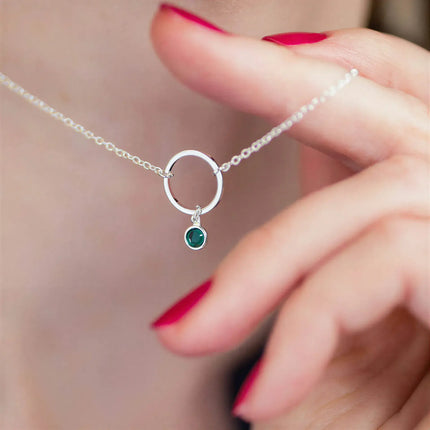 Silver metal chain necklace with a circular ring pendant and a small round green stone charm.