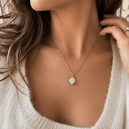 A white druzy gemstone necklace with a gold metal chain worn on a person's neck.