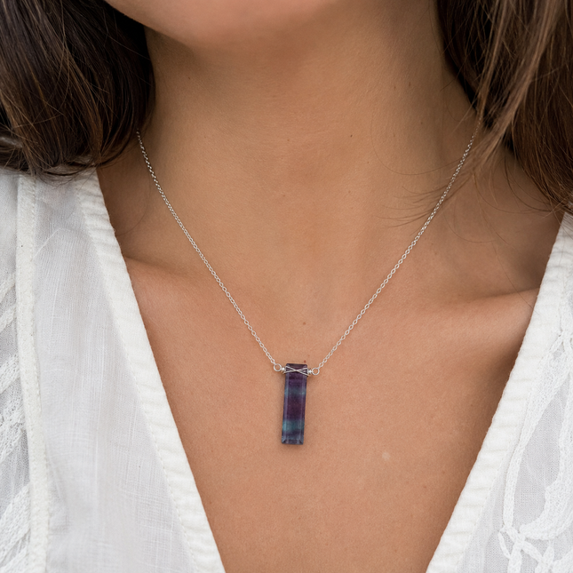 A purple and green rectangular stone bar pendant on a thin silver metal chain worn around a neck.