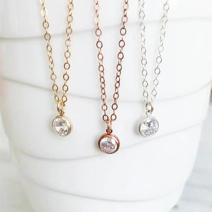Three round CZ necklaces in gold, rose gold, and silver metal finishes hanging against a white textured ceramic surface.