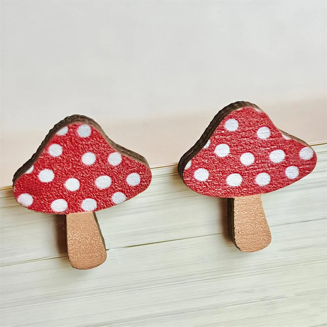 Two red and white polka dot wooden mushroom stud earrings resting on a light-colored surface.