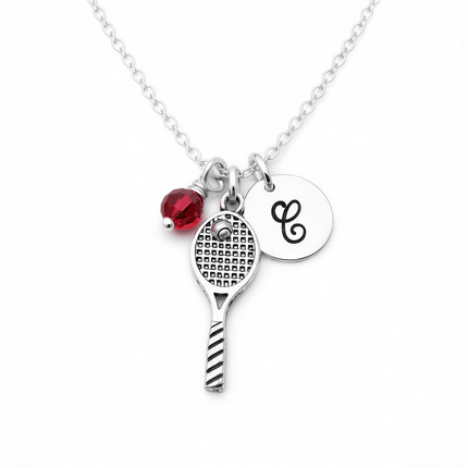 Silver chain necklace with a tennis racquet charm, a red faceted bead, and a round disc engraved with the letter C.