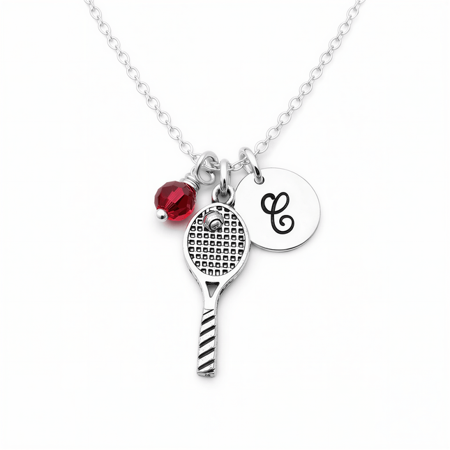 Silver chain necklace with a tennis racquet charm, a red faceted bead, and a round disc engraved with the letter C.
